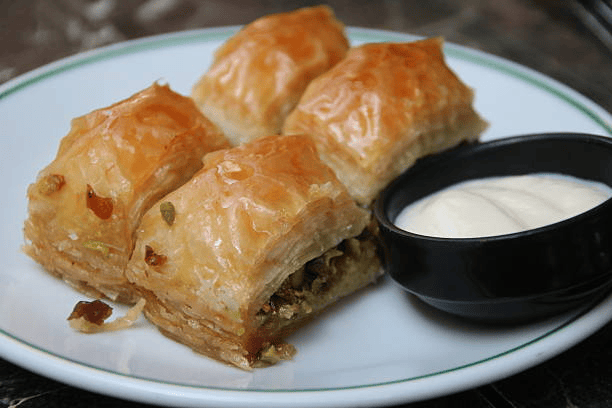 Four golden pistachio-filled pastries beside a bowl of white cream