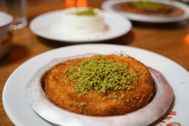 Golden round dessert topped with crushed pistachios on a white plate