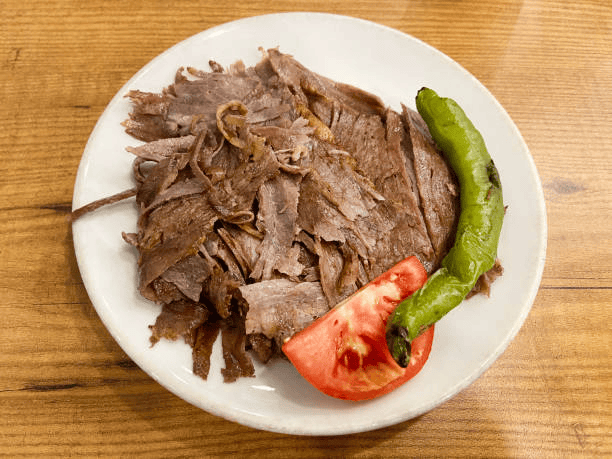 Plate of sliced roasted meat garnished with a green pepper and tomato wedges