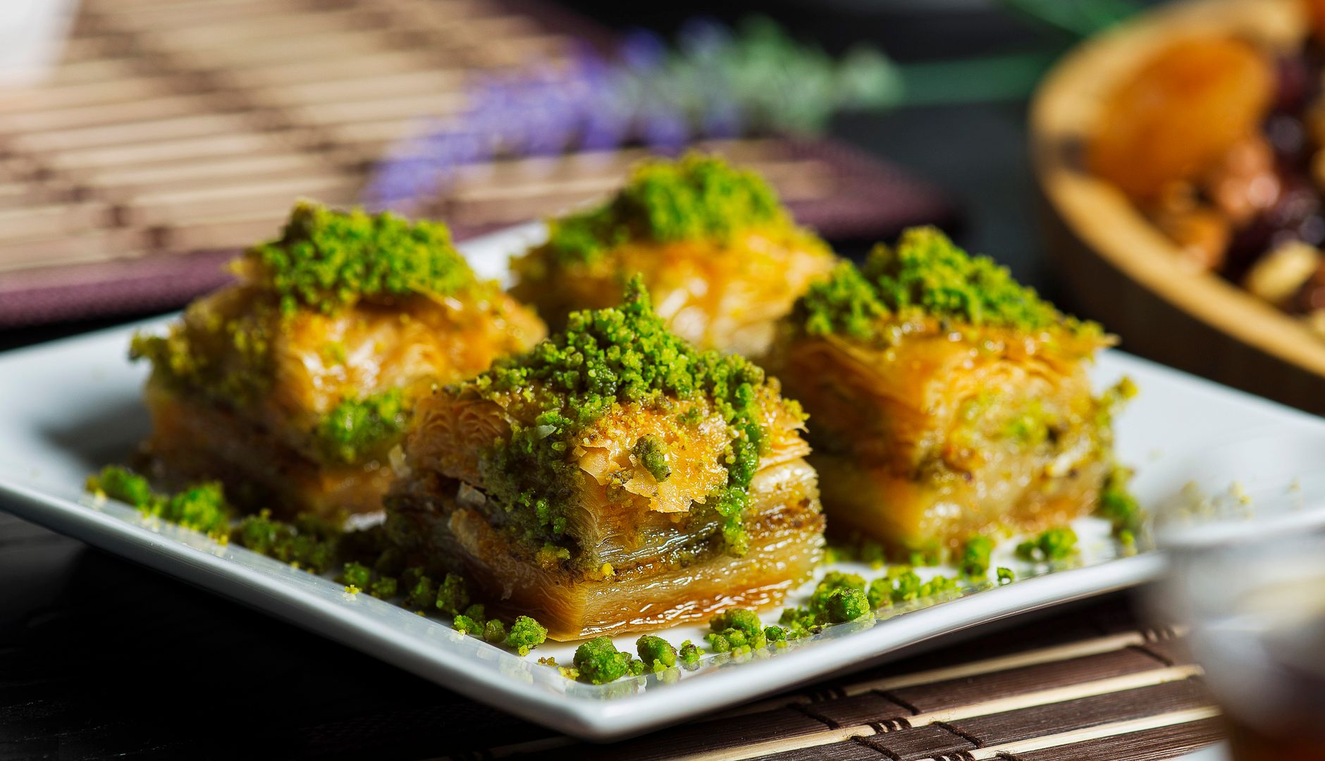 Four pistachio-topped baklava squares on a white platter