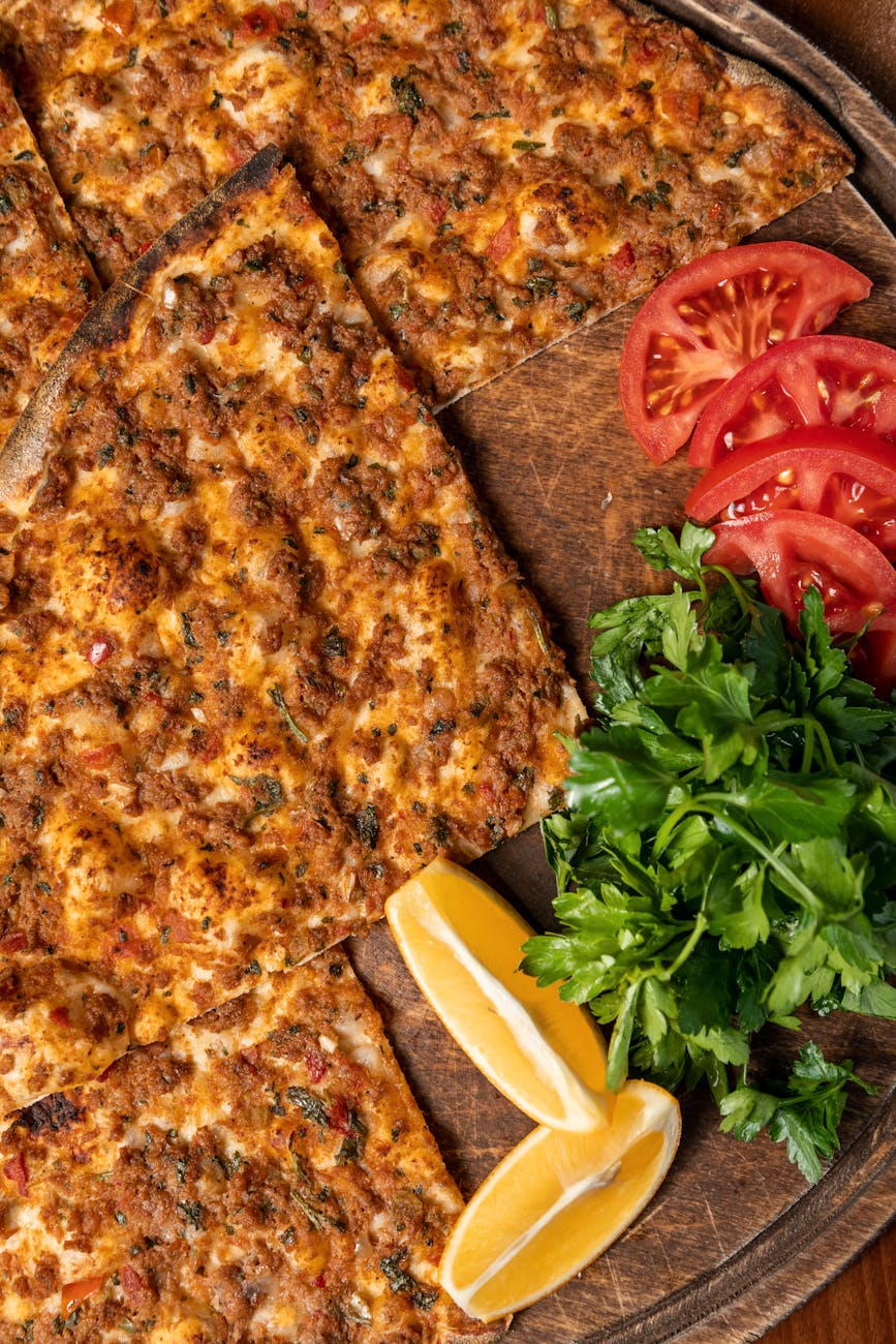pizza sliced lemon parsley and sliced tomato on wooden board