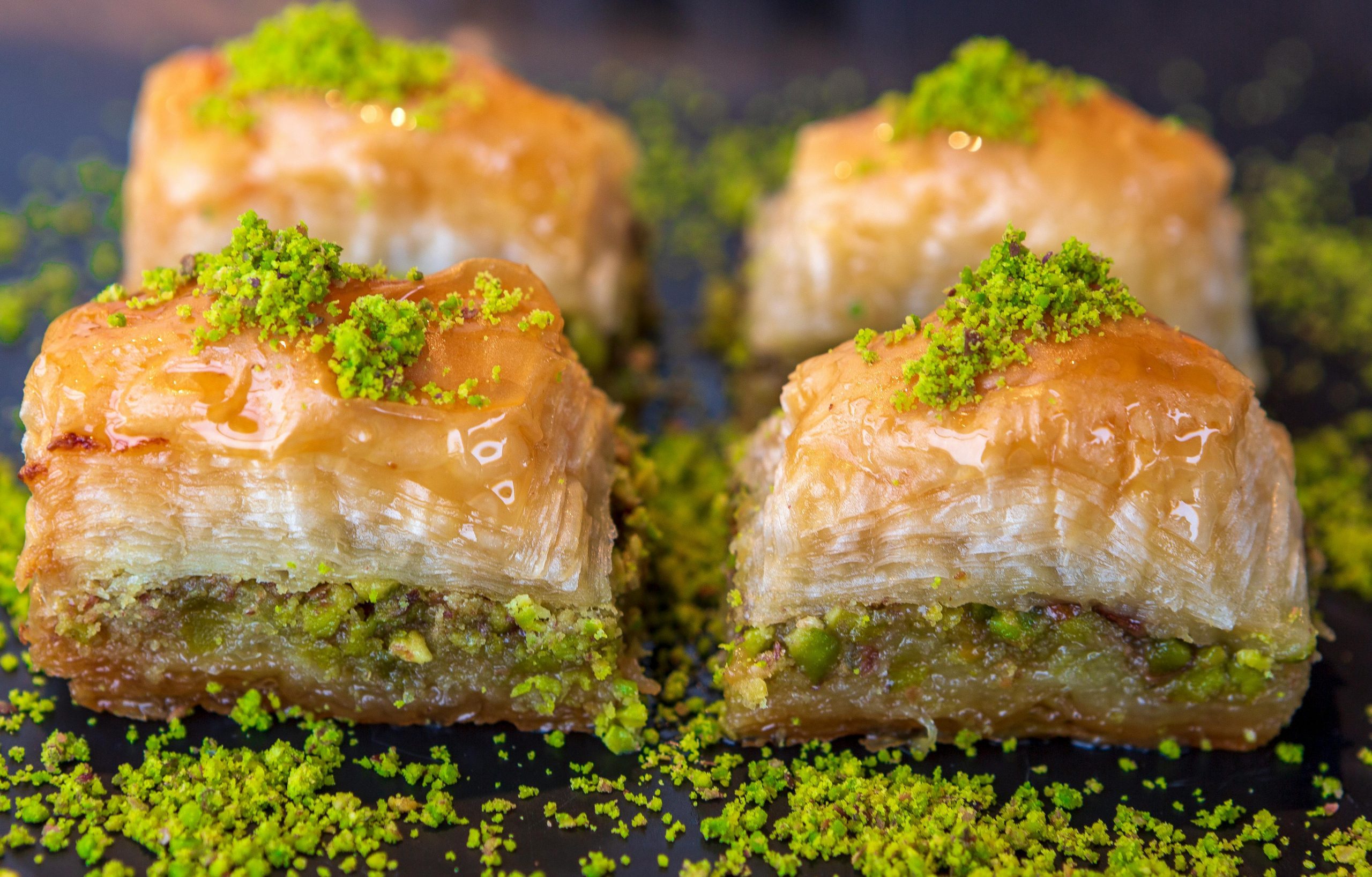 Close-up of freshly made pistachio baklava topped with honey and pistachio crumbs.