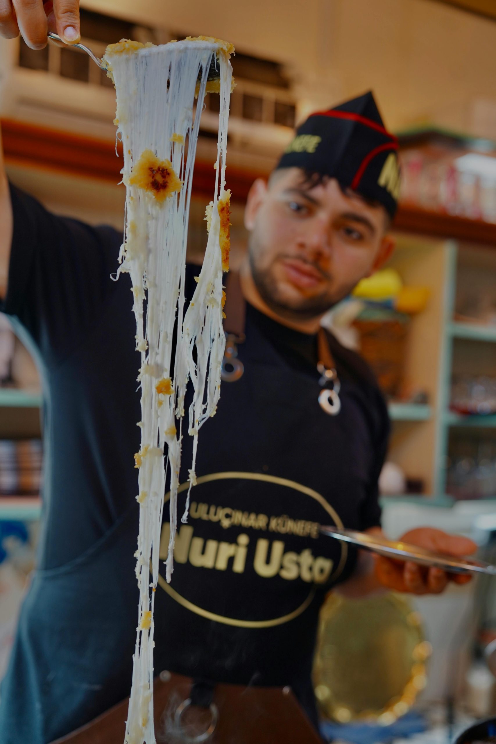 Chef stretching kunefe cheese in Turkish dessert shop.