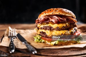 Fresh and juicy hamburger on a paper pillow with beer on a wooden table. Dark background, traditional american food. Junk food
